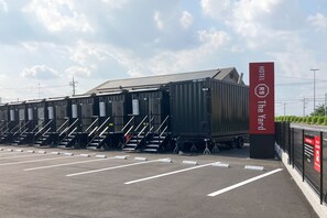 A hotel with a large container-like structure, a parking lot with marked spaces, and a sign indicating the hotel's name. - HOTEL R9 The Yard Hitachiomiya (Hitachiomiya)