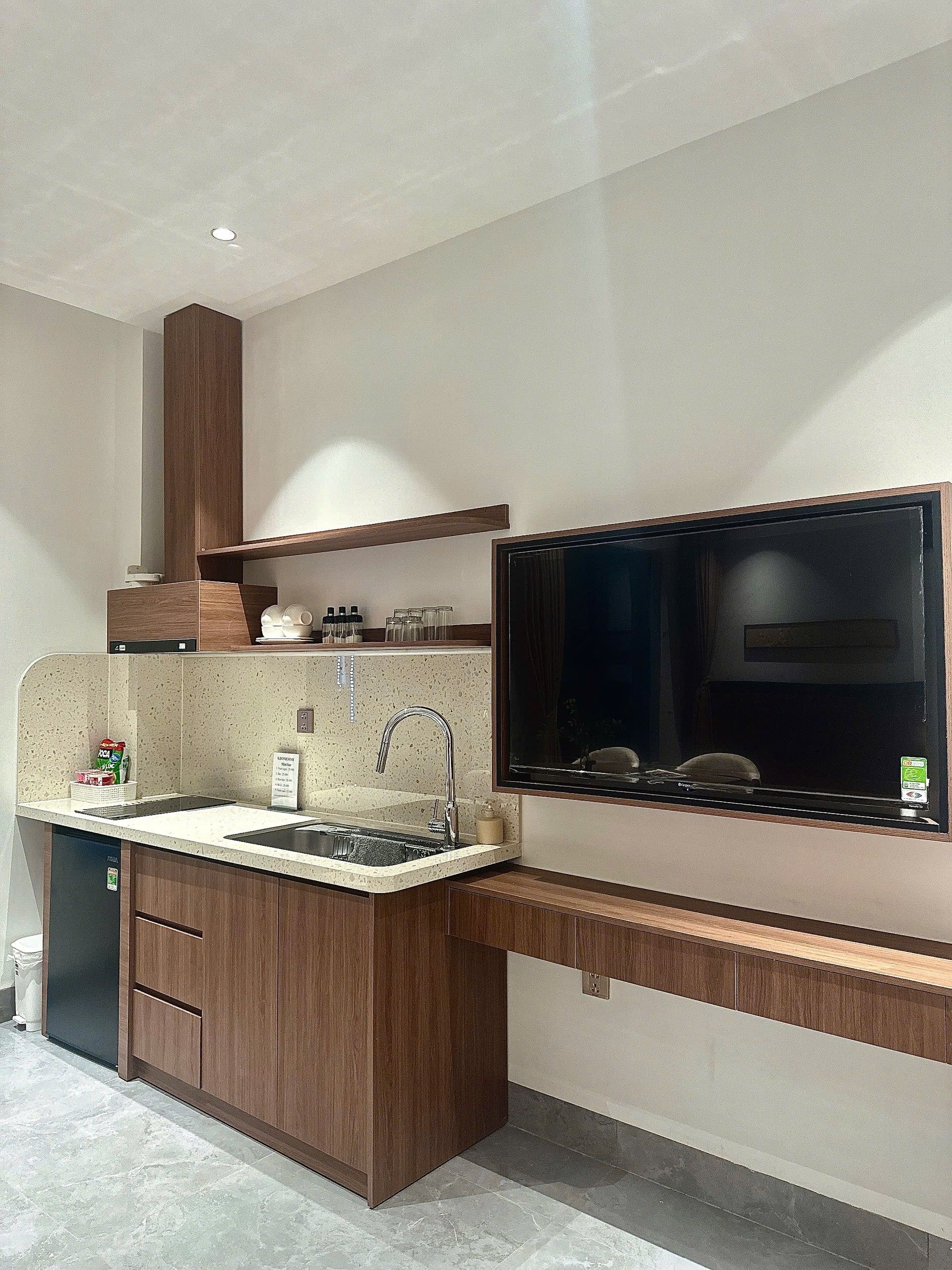 Een moderne keuken met een ingebouwde vaatwasser, een roestvrijstalen spoelbak en een grote flatscreen televisie aan de wand.