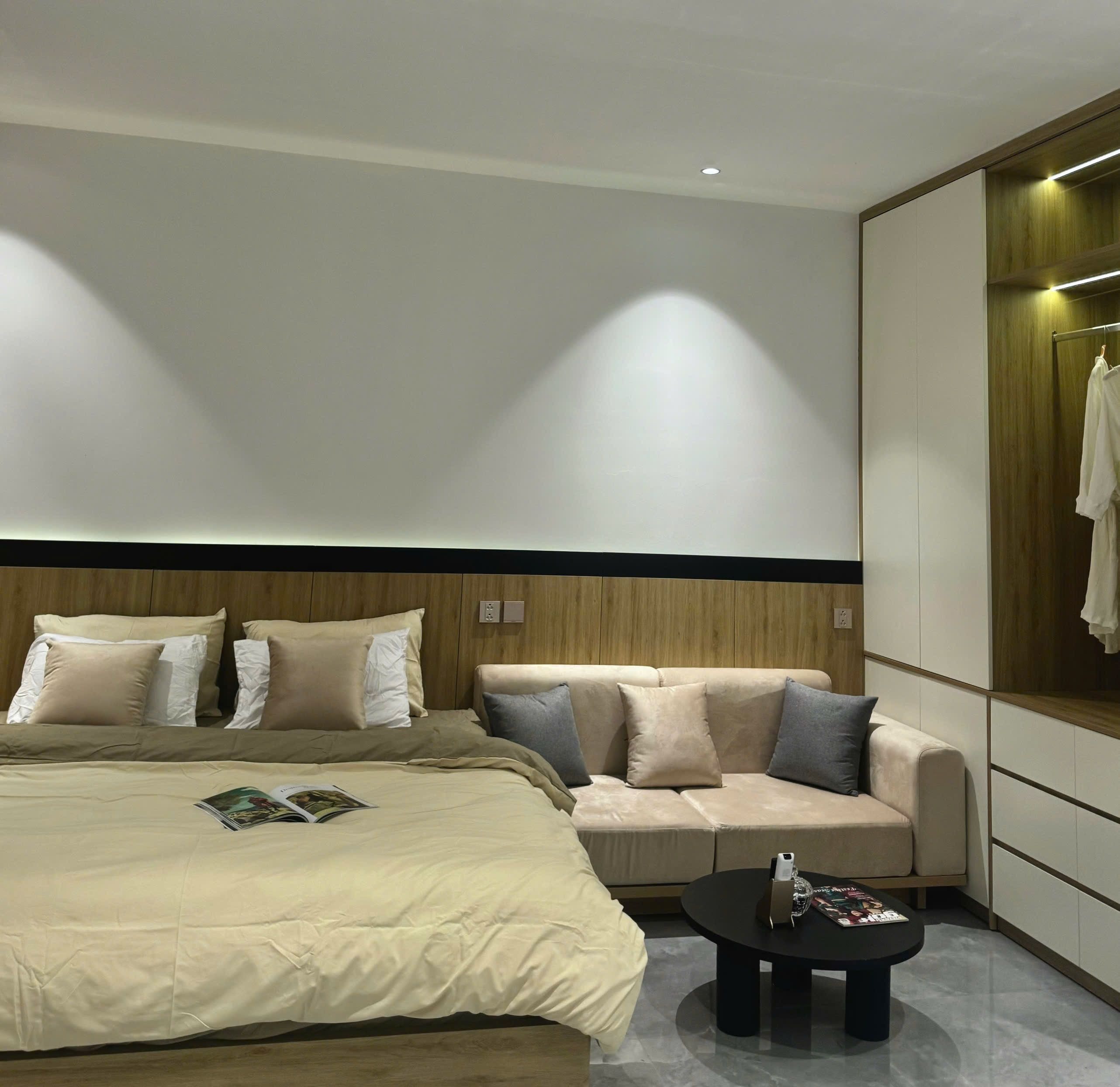 A modern hotel room with a large bed, a sofa, a small table, and a wardrobe.
