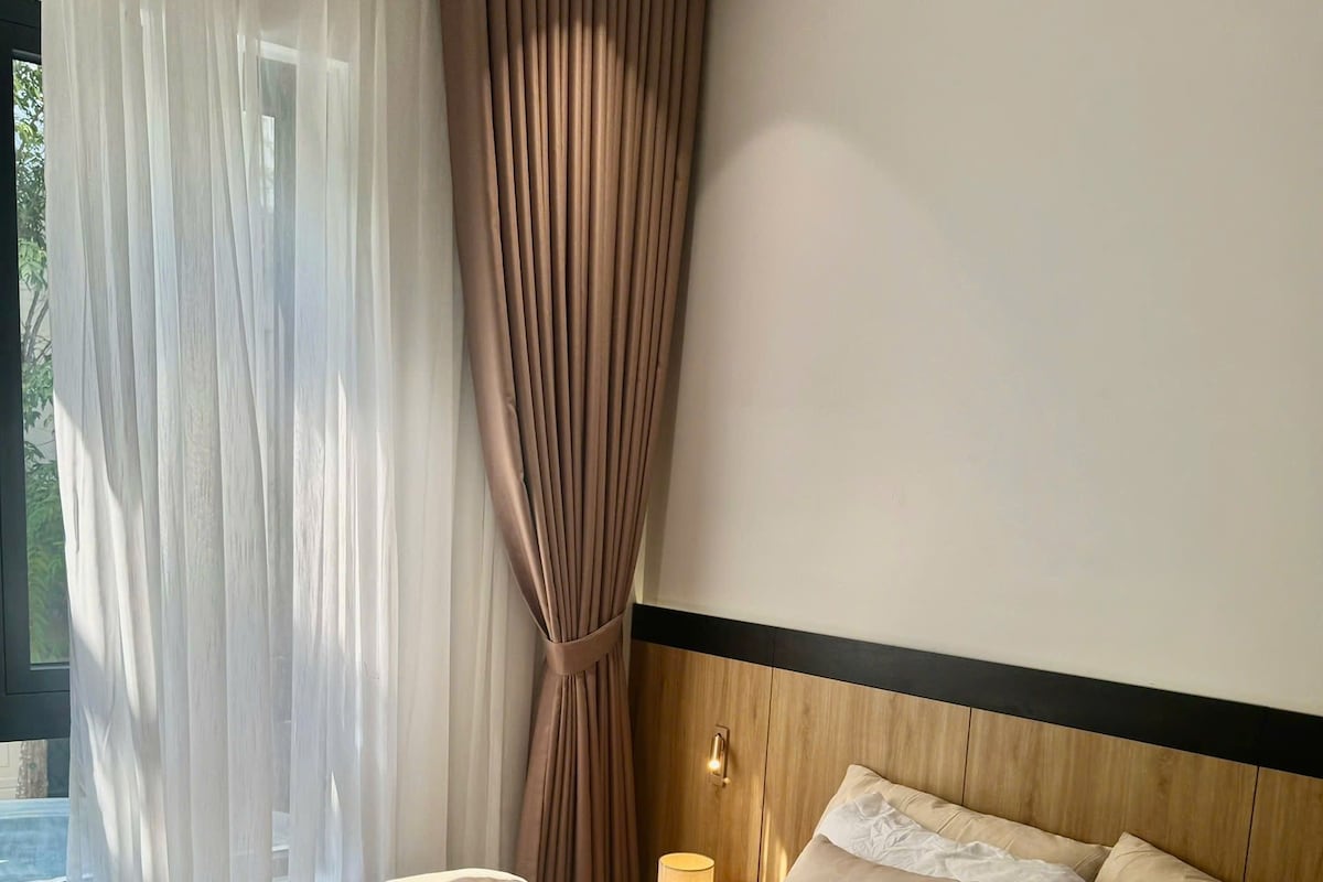 Cama bem arrumada com uma revista, cabeceira de madeira e mesa de cabeceira com abajur.