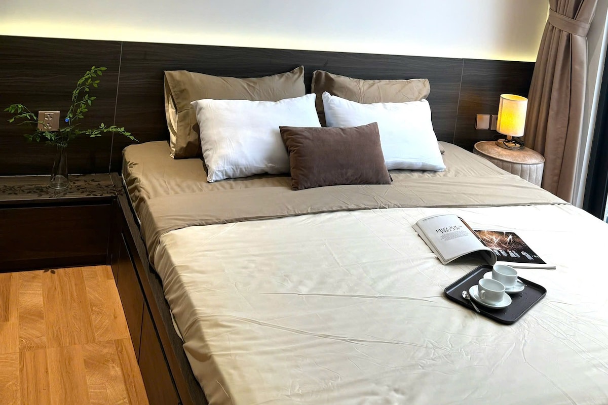 Quarto de hotel com cama, mesa de cabeceira, abajur e bandeja com xícaras.