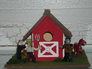 Eine Miniaturlandschaft mit einem roten Bauernhaus, einer Gabel und Figuren eines Mannes, eines Pferdes und einer Person mit Helm.