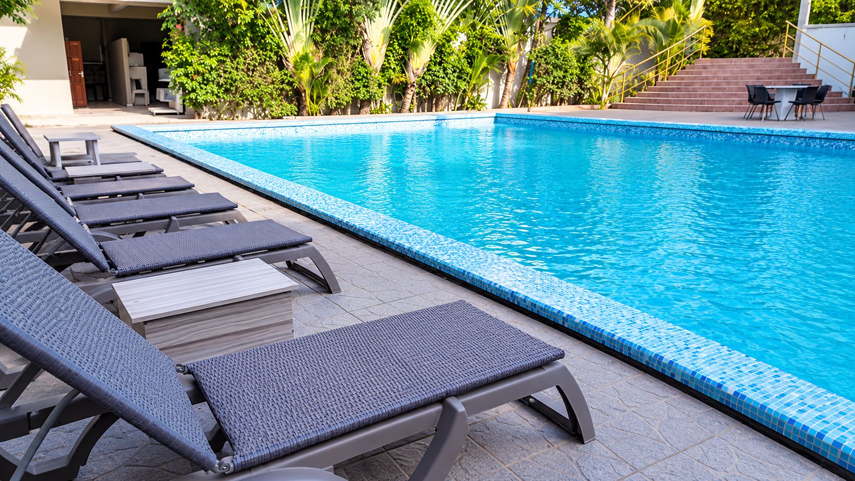 A swimming pool with lounge chairs and a tiled deck.