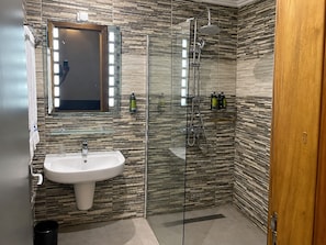 A modern bathroom with a glass shower enclosure, a white sink, and a mirror above it. - Hotel Copacabana Beach Kribi  (Kribi)