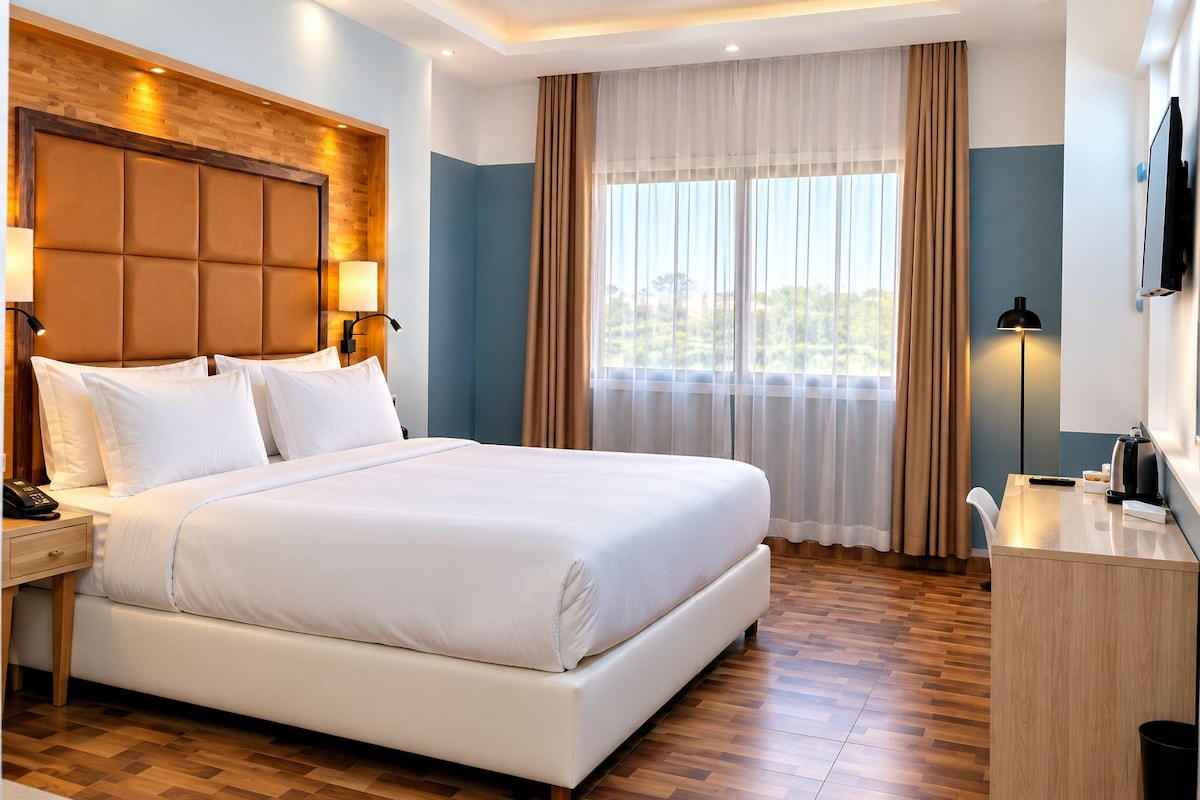 A hotel room with a large bed, a desk, a TV, and a window with curtains.