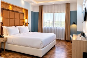 A hotel room with a large bed, a desk, a TV, and a window with curtains. - Hotel Copacabana Beach Kribi  (Kribi)