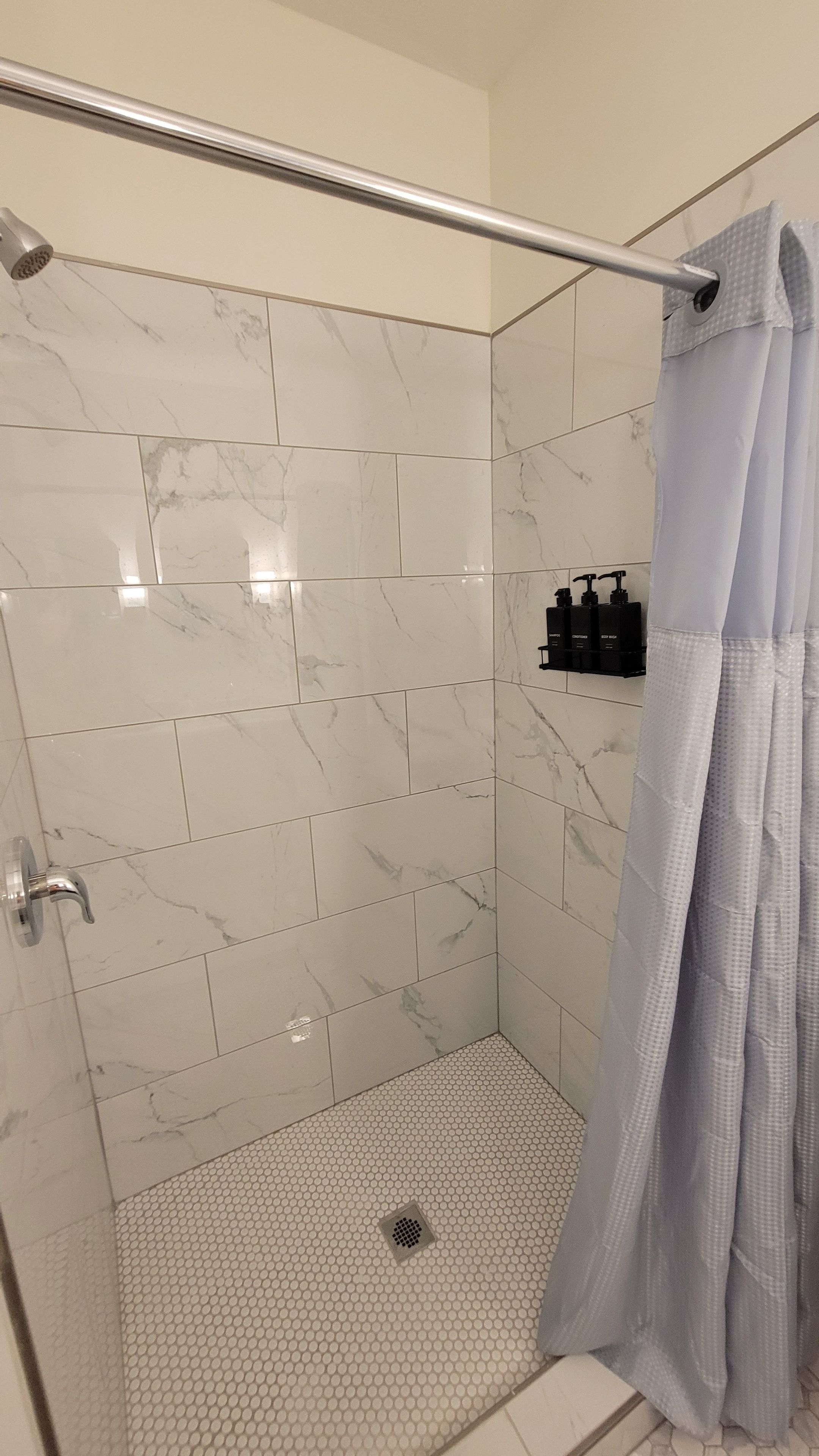 A shower area with a glass door, white marble tiles, and a showerhead.