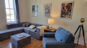 Ein Wohnzimmer mit einem Ecksofa, einem kleinen Hocker, einer Lampe und einem Teleskop auf einem Stativ.