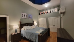 Ein Schlafzimmer mit einem Bett, zwei Nachttischen, einer Kommode, einem Deckenventilator und einer Wand-Klimaanlage.