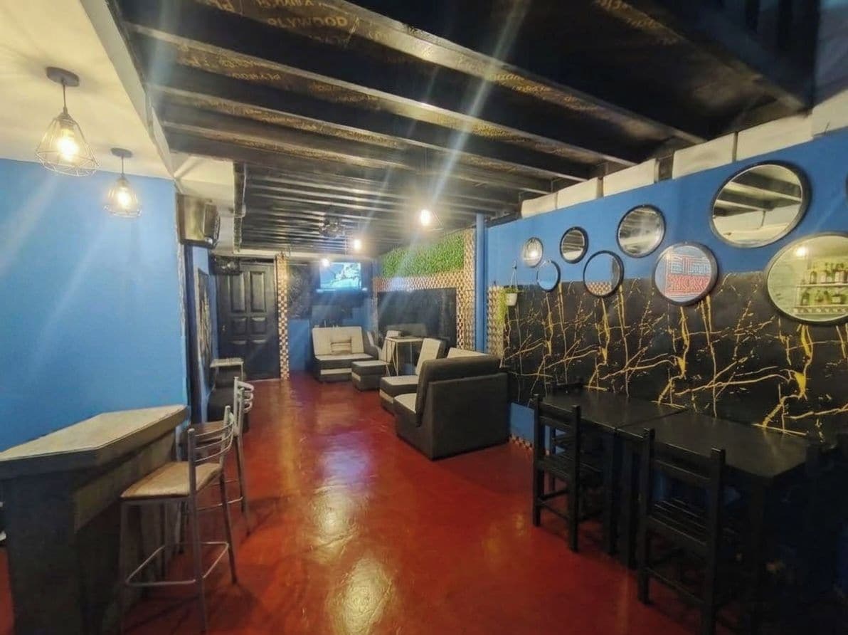 Un'area bar con posti a sedere e un bancone, una parete blu con specchi circolari e un pavimento rosso.