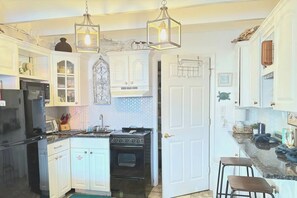 Una cocina con armarios blancos, un refrigerador negro, una estufa y lámparas colgantes.
