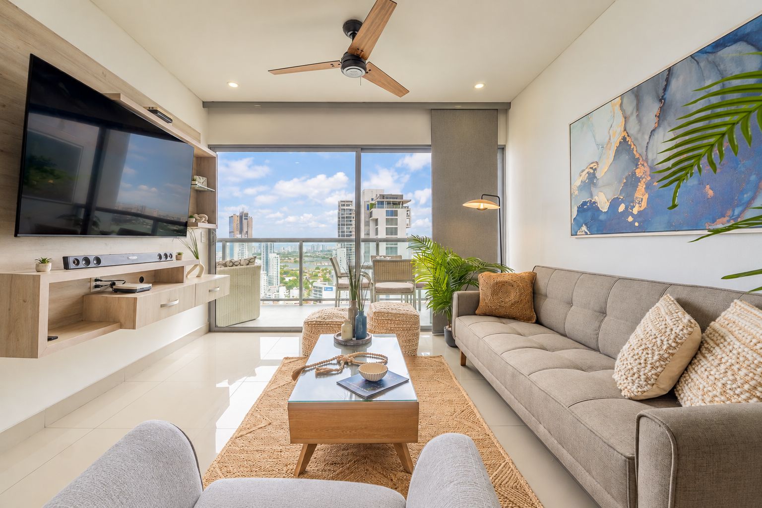 Ein modernes Wohnzimmer mit einem Flachbildfernseher, einem Deckenventilator, einer Couch und einem großen Fenster mit Blick auf die Stadt.