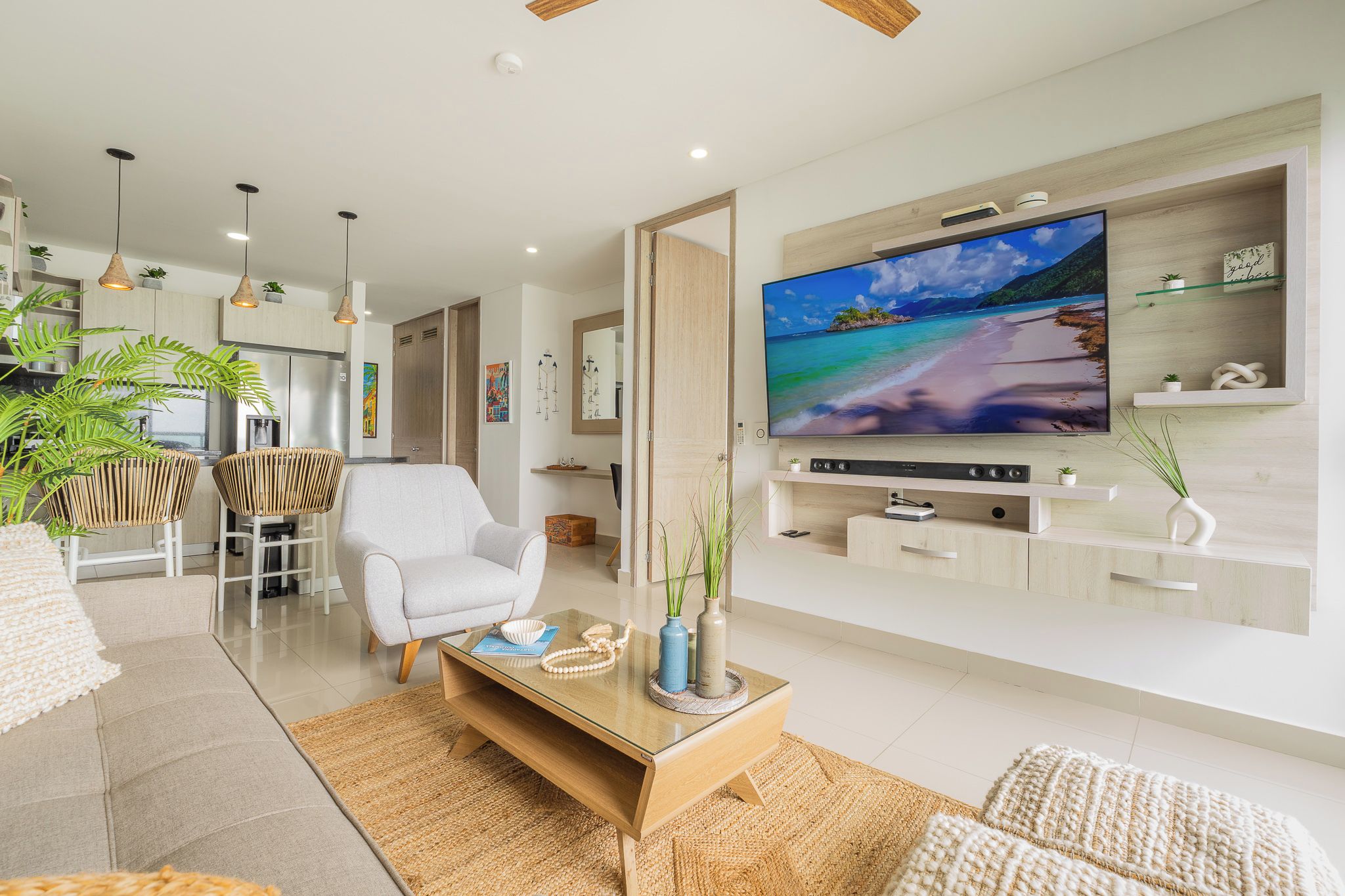 Ein modernes Wohnzimmer mit Fernseher, bequemen Sitzmöglichkeiten und einer Küche im Hintergrund.