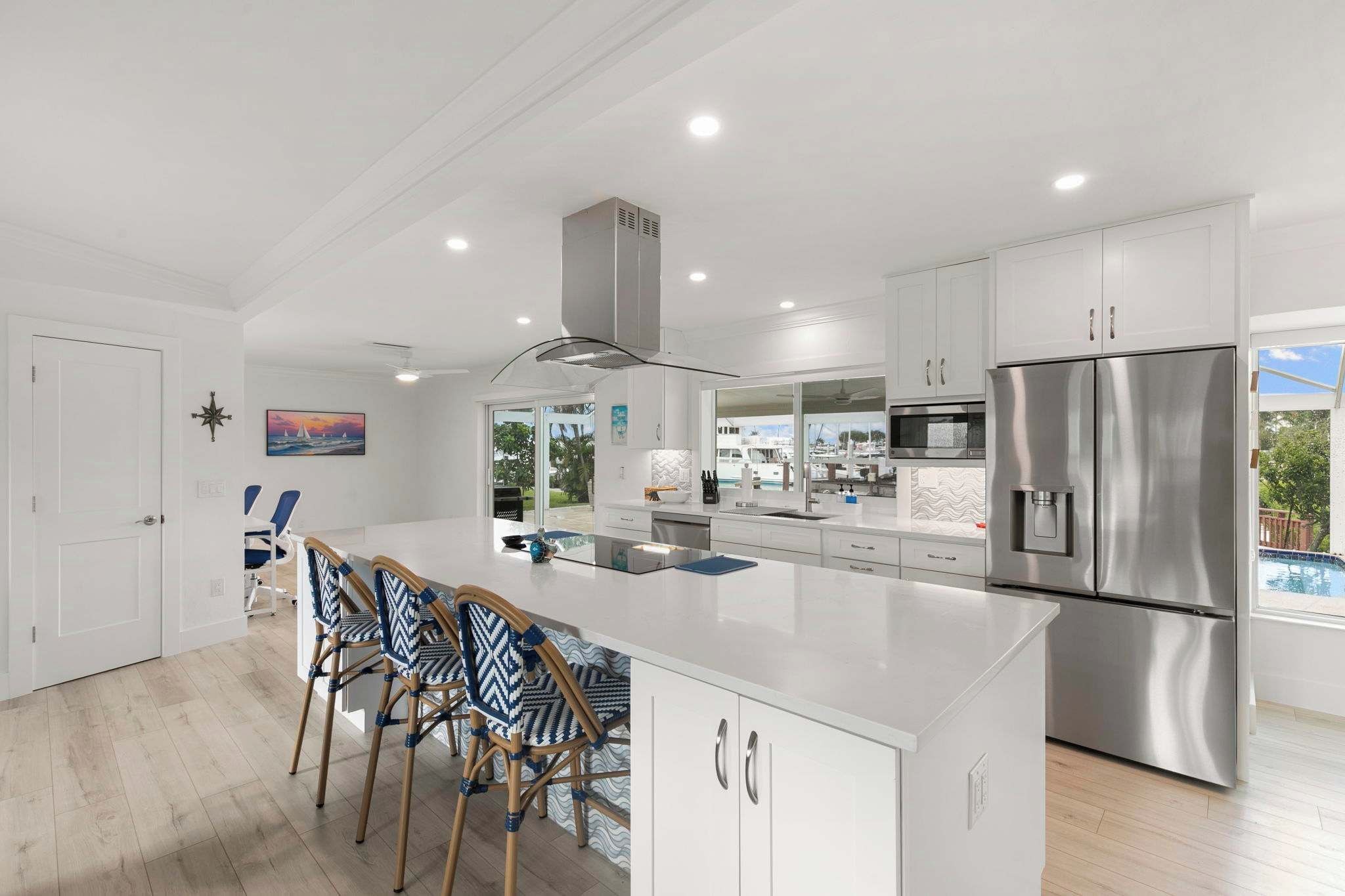 A modern kitchen with white cabinetry, a stainless steel refrigerator, and a dining area with wicker chairs.