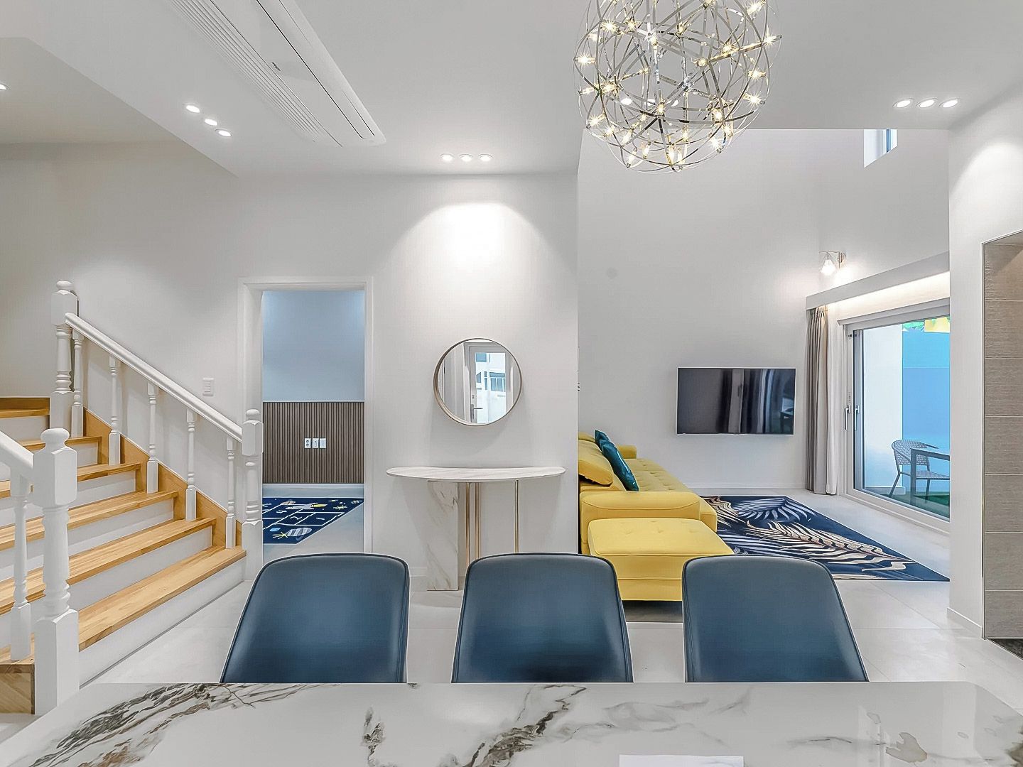 A modern living room with a staircase, a round mirror, a sofa, and a flat-screen TV.
