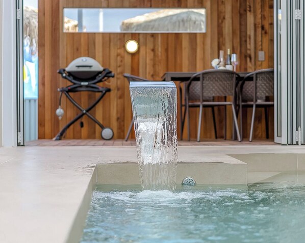 A water feature in a pool area with a wooden wall and outdoor furniture in the background. - Hian Private Pool Villa (Gyeongju)