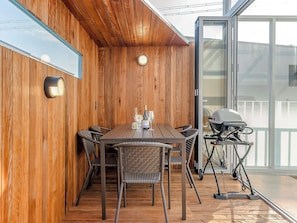Una habitación con paneles de madera, una mesa de comedor, sillas, una parrilla y un gran ventanal corredizo.