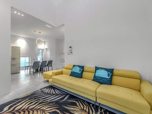 Una sala de estar moderna con un sofá amarillo, un tapete estampado y un comedor con sillas y una mesa.
