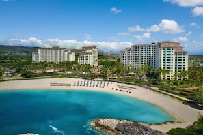 Un hotel frente a la playa con varios edificios altos, una playa de arena y un mar azul cristalino.