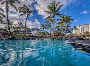 Une piscine entourée de palmiers et un bâtiment d’hôtel.