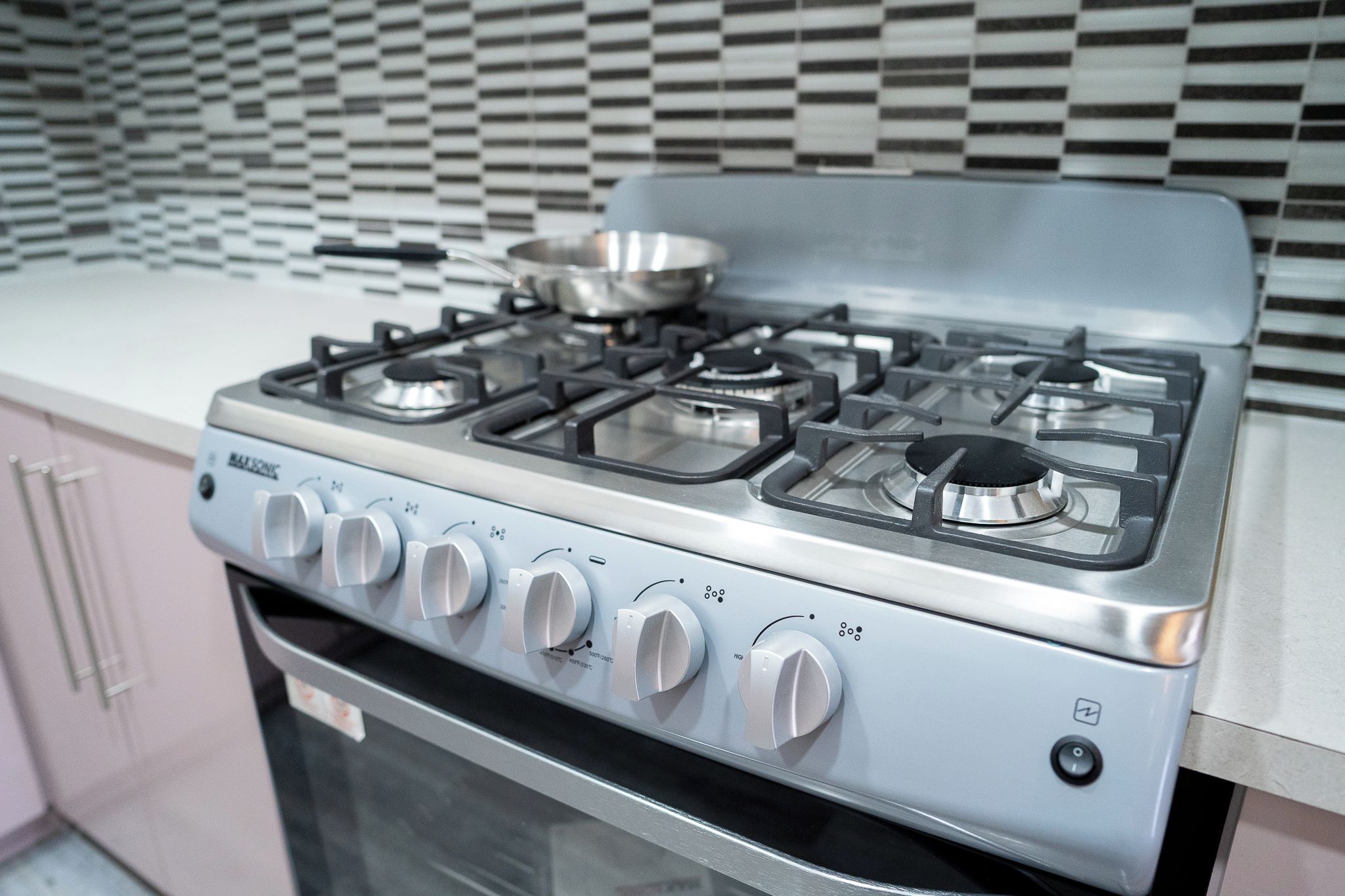 A kitchen with a stainless steel stove, a pot on the burner, and a checkered backsplash.