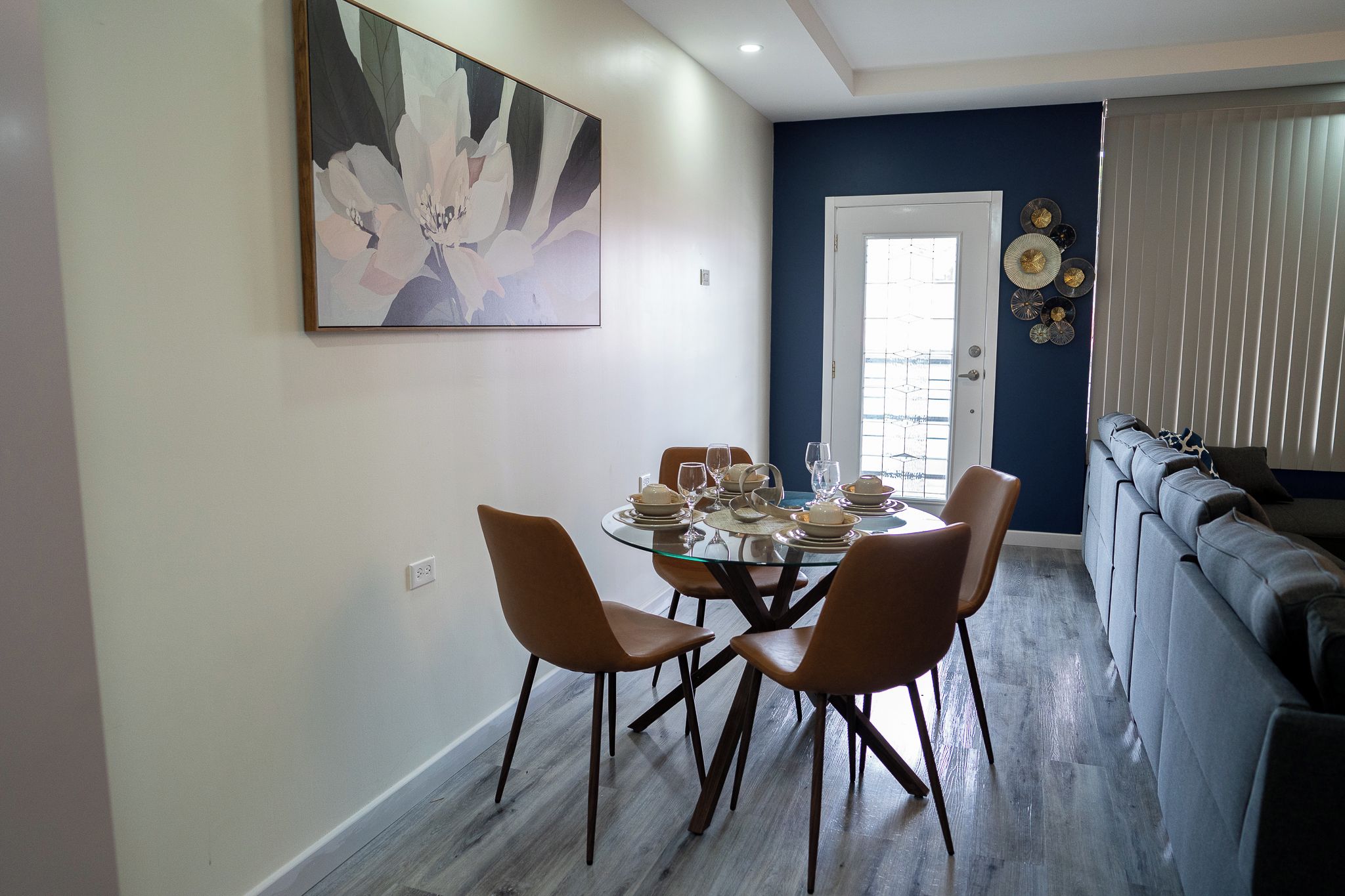 Een eetgedeelte met een glazen tafel, vier stoelen en een schilderij aan de muur.