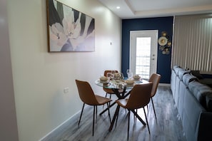 Un comedor con una mesa de vidrio, cuatro sillas y un cuadro en la pared.