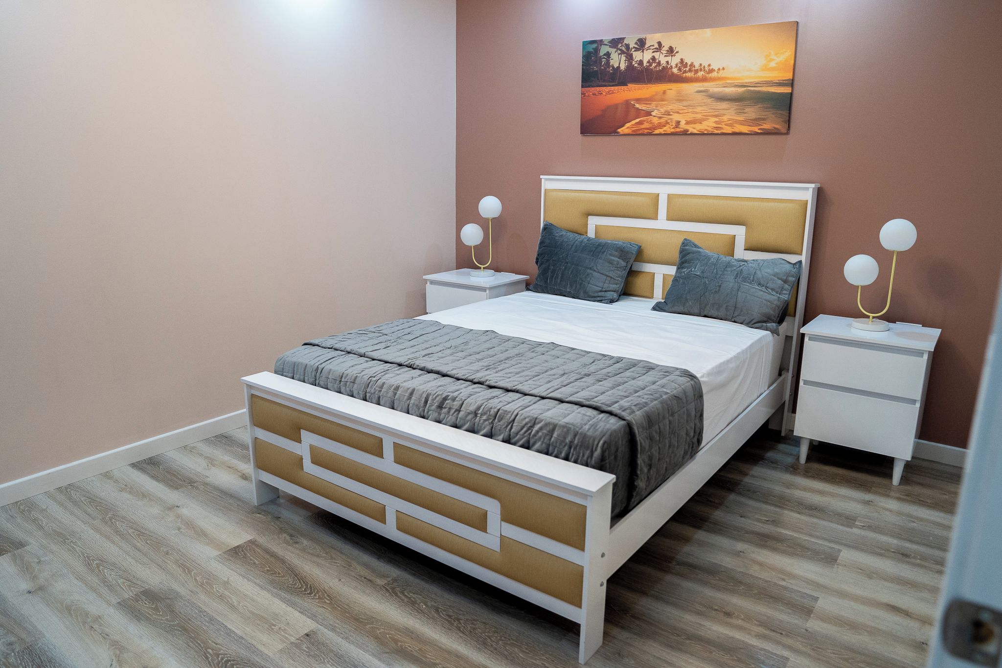 A bedroom with a bed, nightstands, a wall-mounted lamp, and a painting.