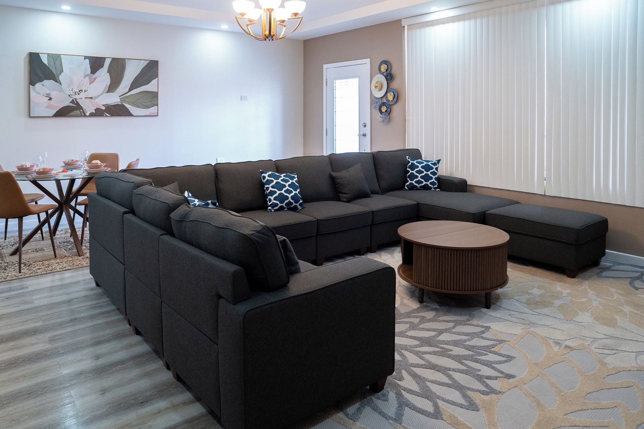 A modern living room with a sectional sofa, a round coffee table, and a dining area with a glass table and chairs.
