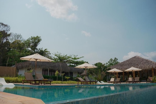 A swimming pool with lounge chairs and umbrellas, surrounded by thatched-roof structures. - The Beach Resort (Koh Rong island)