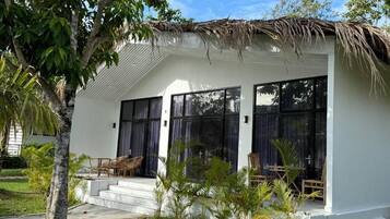 Una casa moderna con techo de paja, ventanas grandes y un pequeño espacio de estar al aire libre.