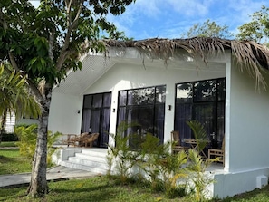 A modern house with a thatched roof, large windows, and a small outdoor seating area. - The Beach Resort (Koh Rong island)
