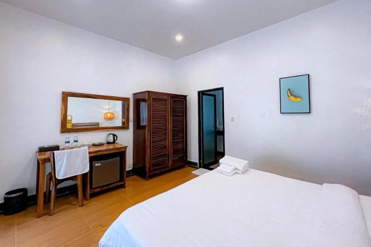 A hotel room with a bed, a desk with a mirror, a wardrobe, and a door.