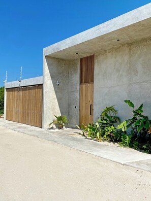 A modern building with a concrete facade, a wooden door, and a small garden area with various plants. - New Listing (Progreso)