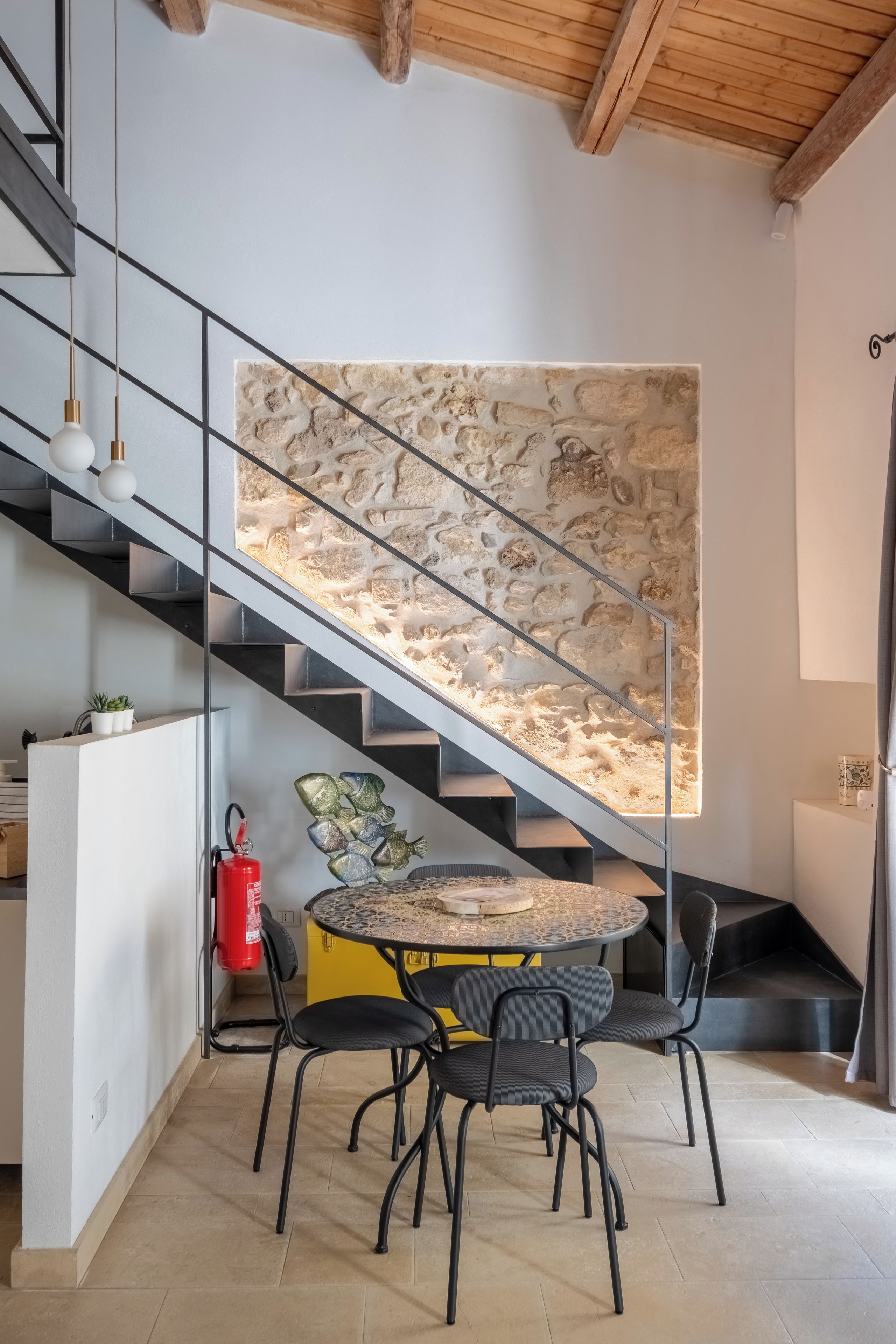 Un intérieur moderne avec un escalier, une table ronde entourée de chaises et un mur décoratif.