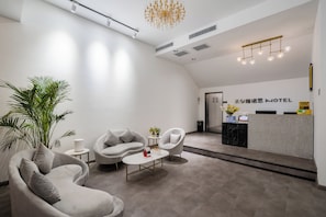 Een moderne hotel lobby met een receptiebalie, een zithoek en een grote plant.