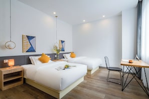 Een hotelkamer met twee bedden, een bureau en een stoel. Er hangen twee schilderijen aan de muur, een vaas met bloemen staat er, en een lamp op het nachtkastje.
