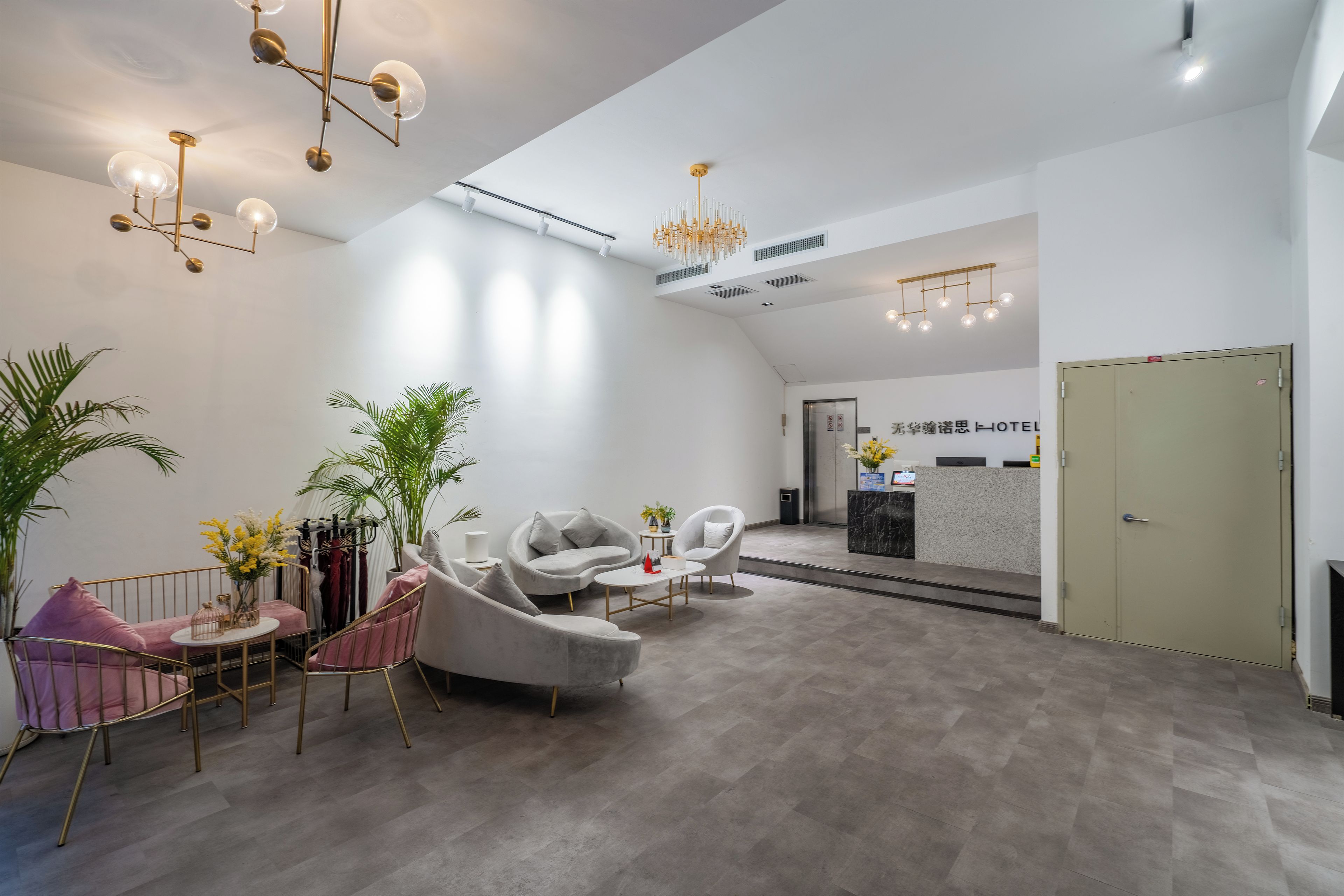 A hotel reception area with a modern design, featuring a reception desk, seating area with chairs, and a chandelier.
