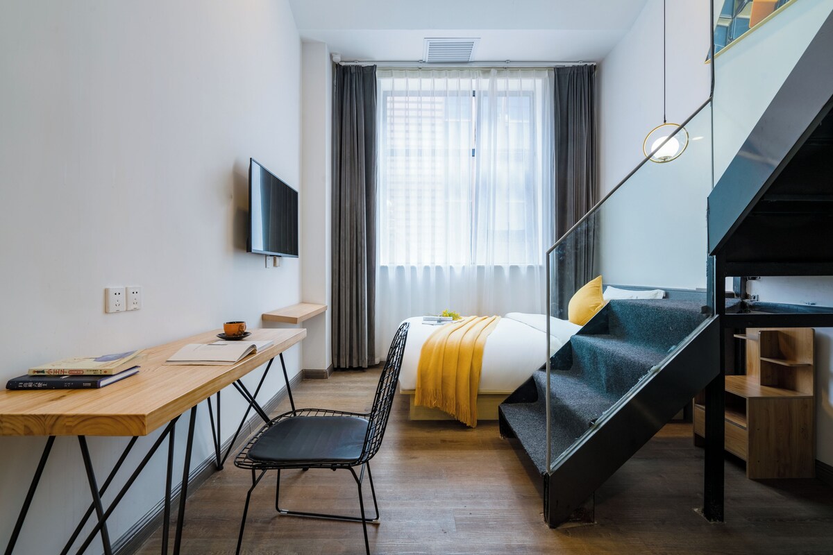 Een kleine hotelkamer met een bed, een bureau, een stoel, een televisie en een trap.