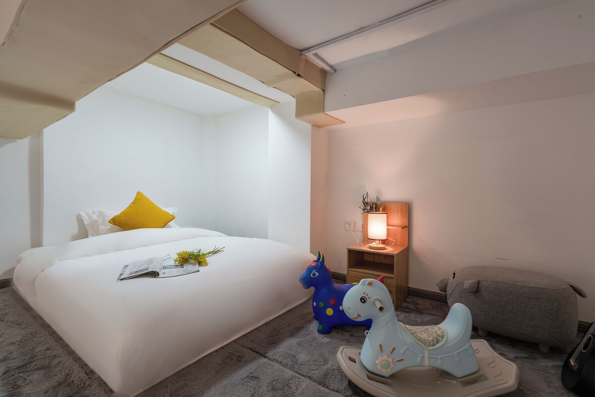A bedroom with a bed, a nightstand, a lamp, and a rocking horse.
