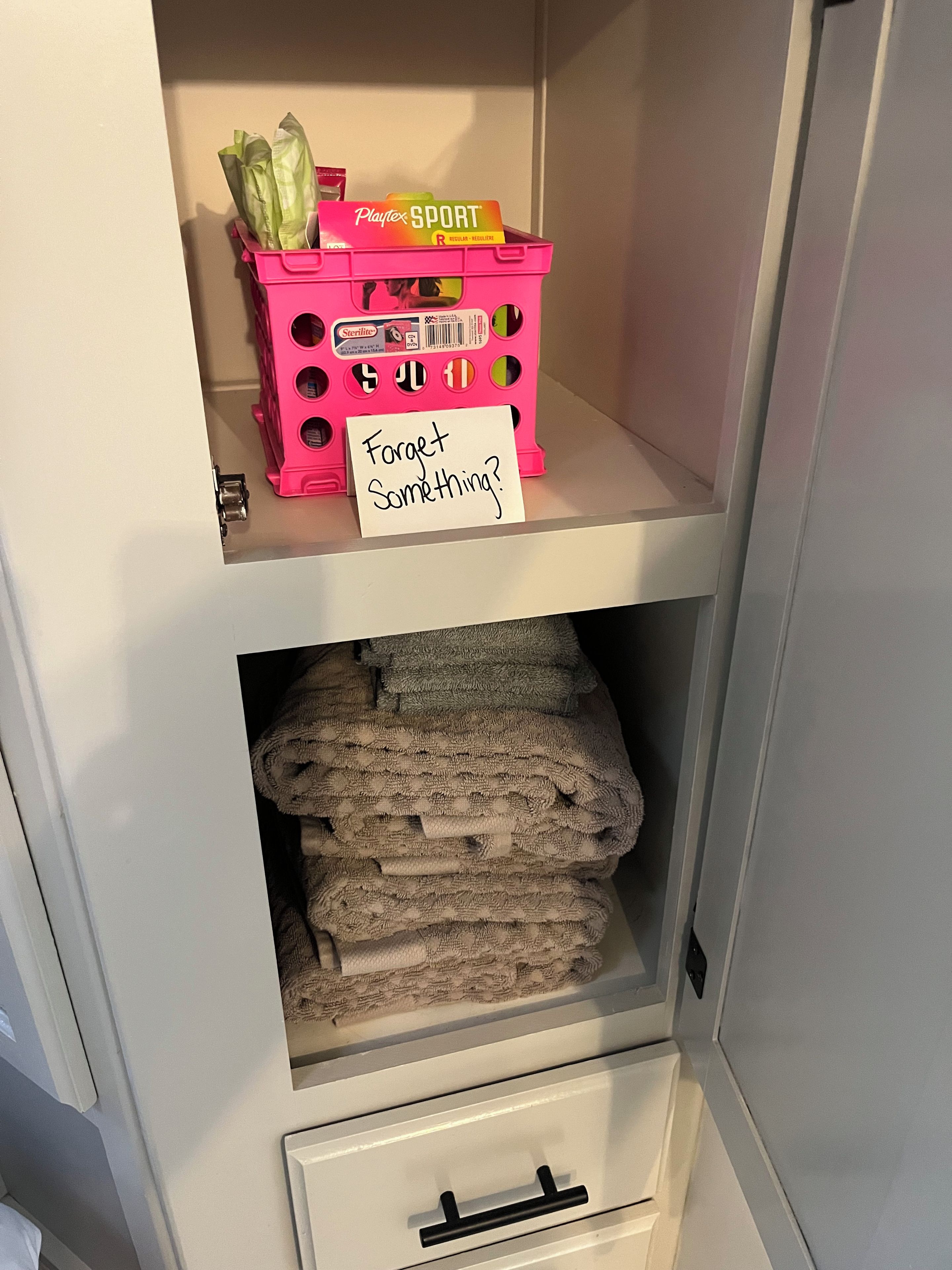 A storage unit with a pink basket containing items and a note on the shelf.