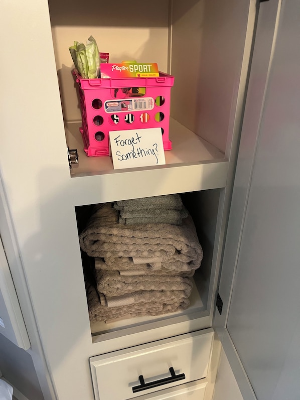 Un espace de rangement avec un panier rose contenant des objets et un mot posé sur l’étagère.