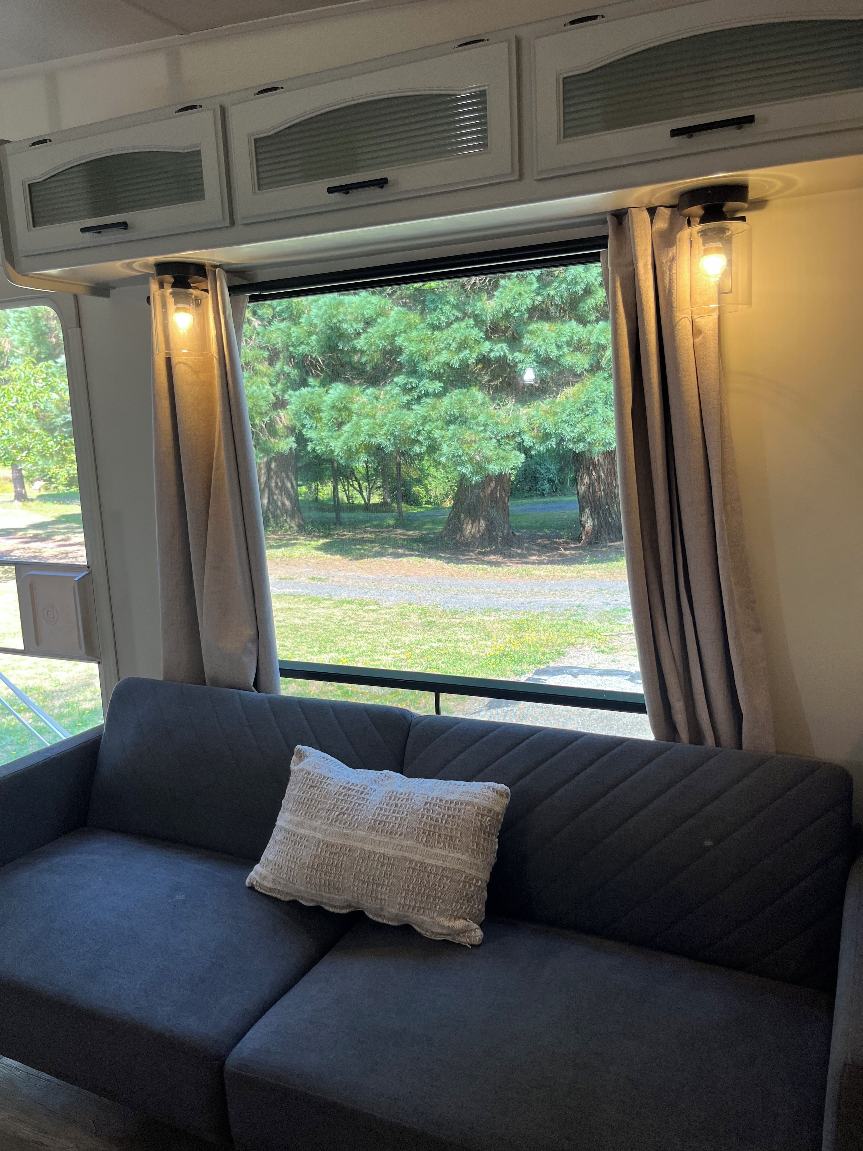 Habitació amb un sofà, una finestra amb cortines i vista a arbres.