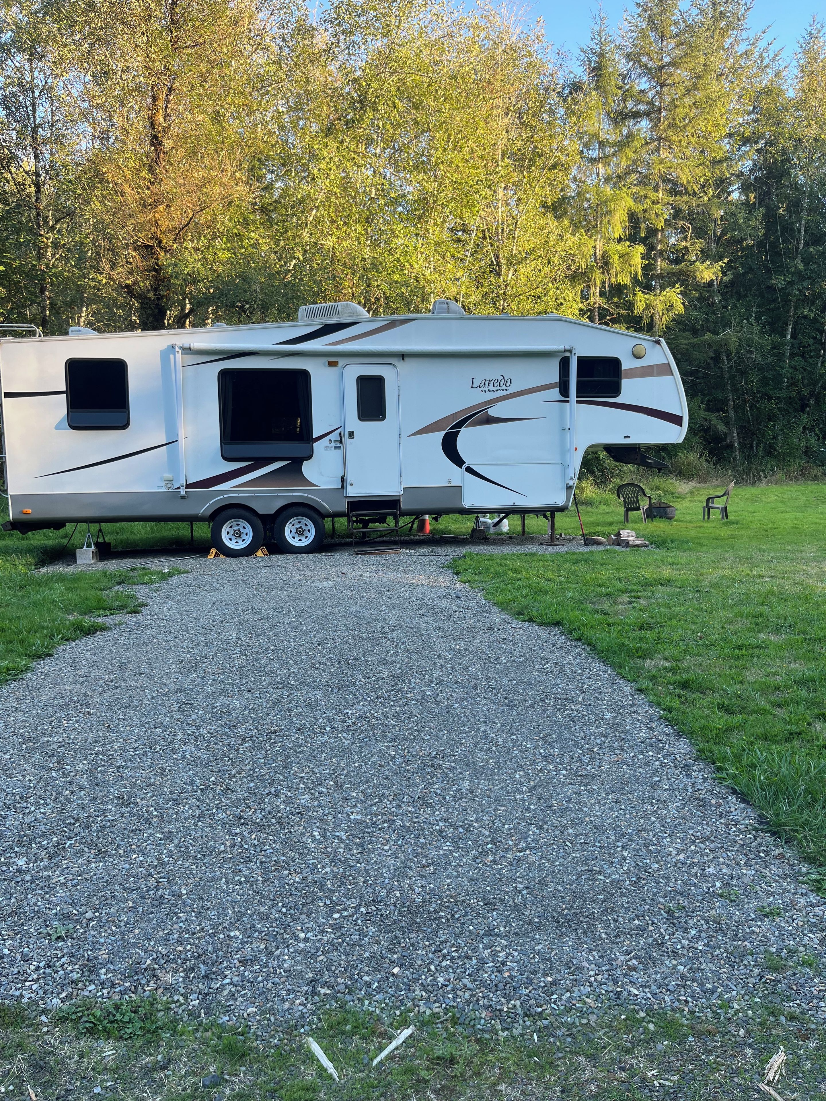 A recreational vehicle parked on a gravel path with a grassy area and trees in the background.