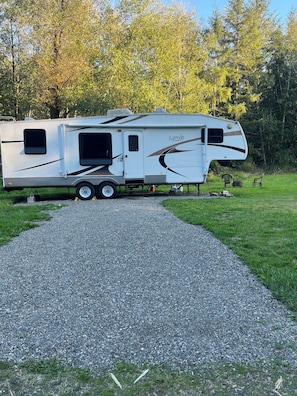 En fritstående campingvogn parkeret på en grusvej med græs og træer i baggrunden.