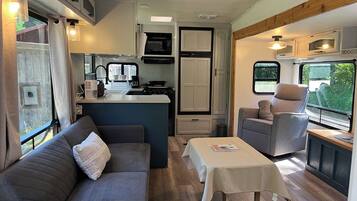 Interior d'una autocaravana compacta amb cuina americana, sofà, taula i finestra.