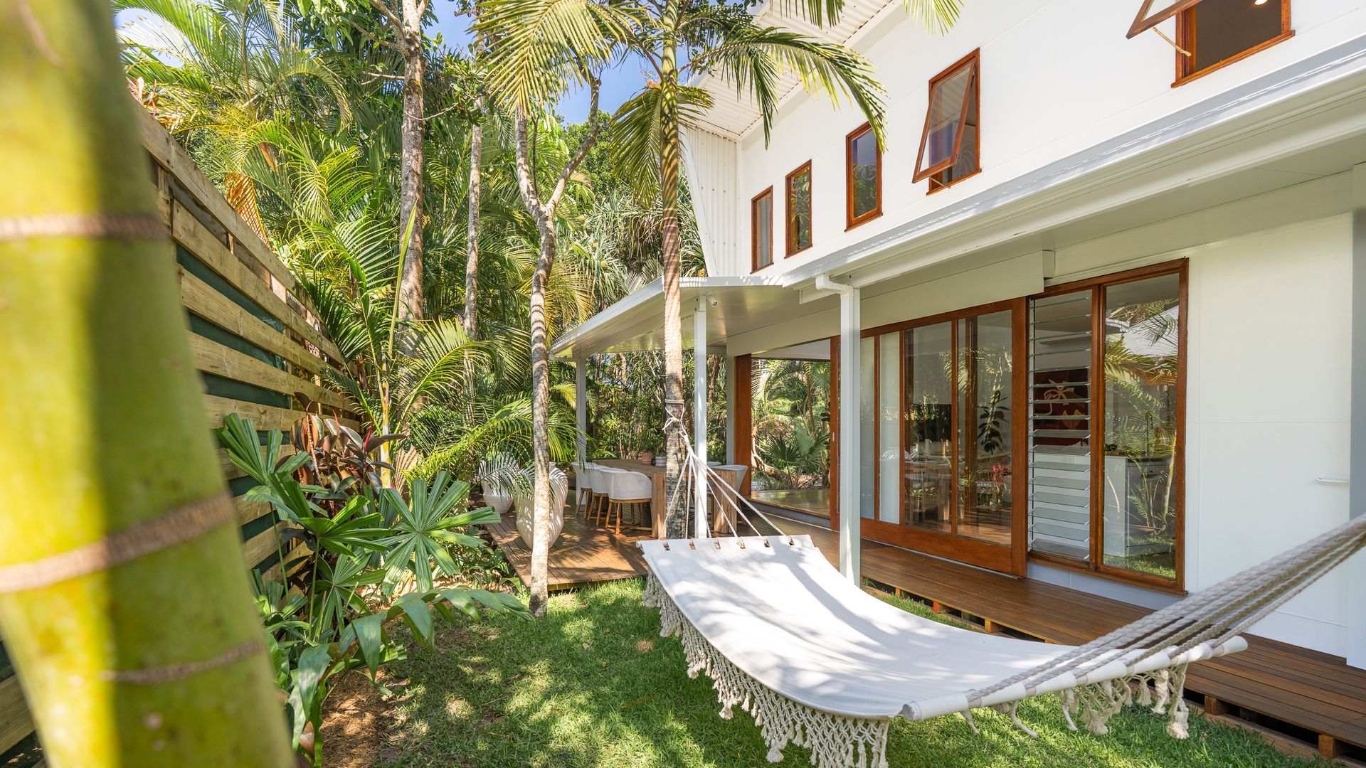 Un bâtiment blanc doté de grandes fenêtres, d’un hamac et d’une végétation tropicale luxuriante.