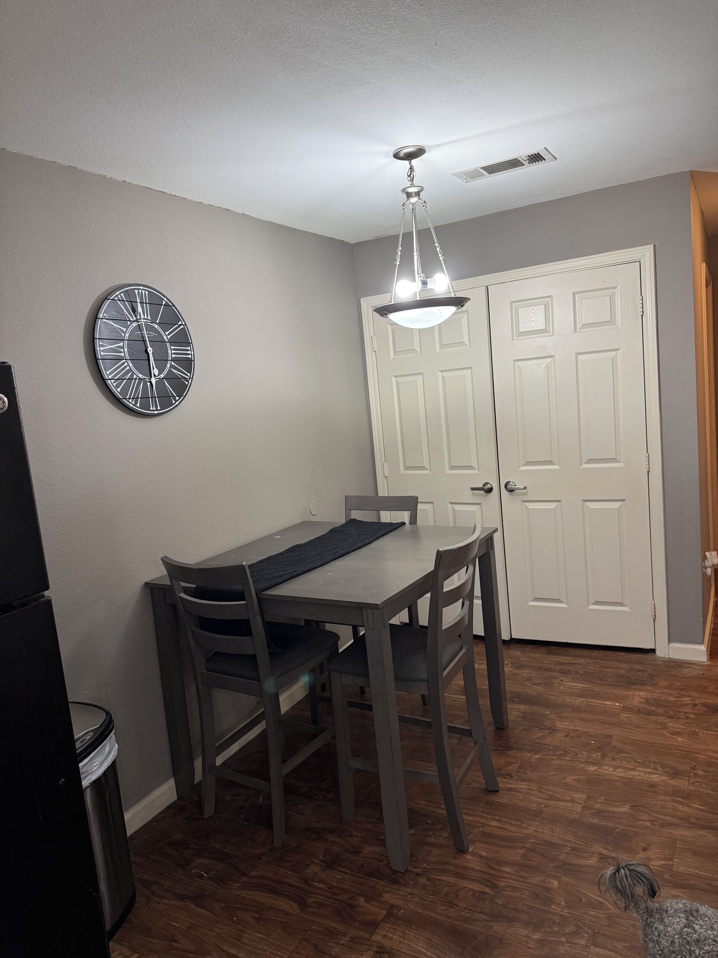 A dining area with a table, chairs, a wall clock, and a door.