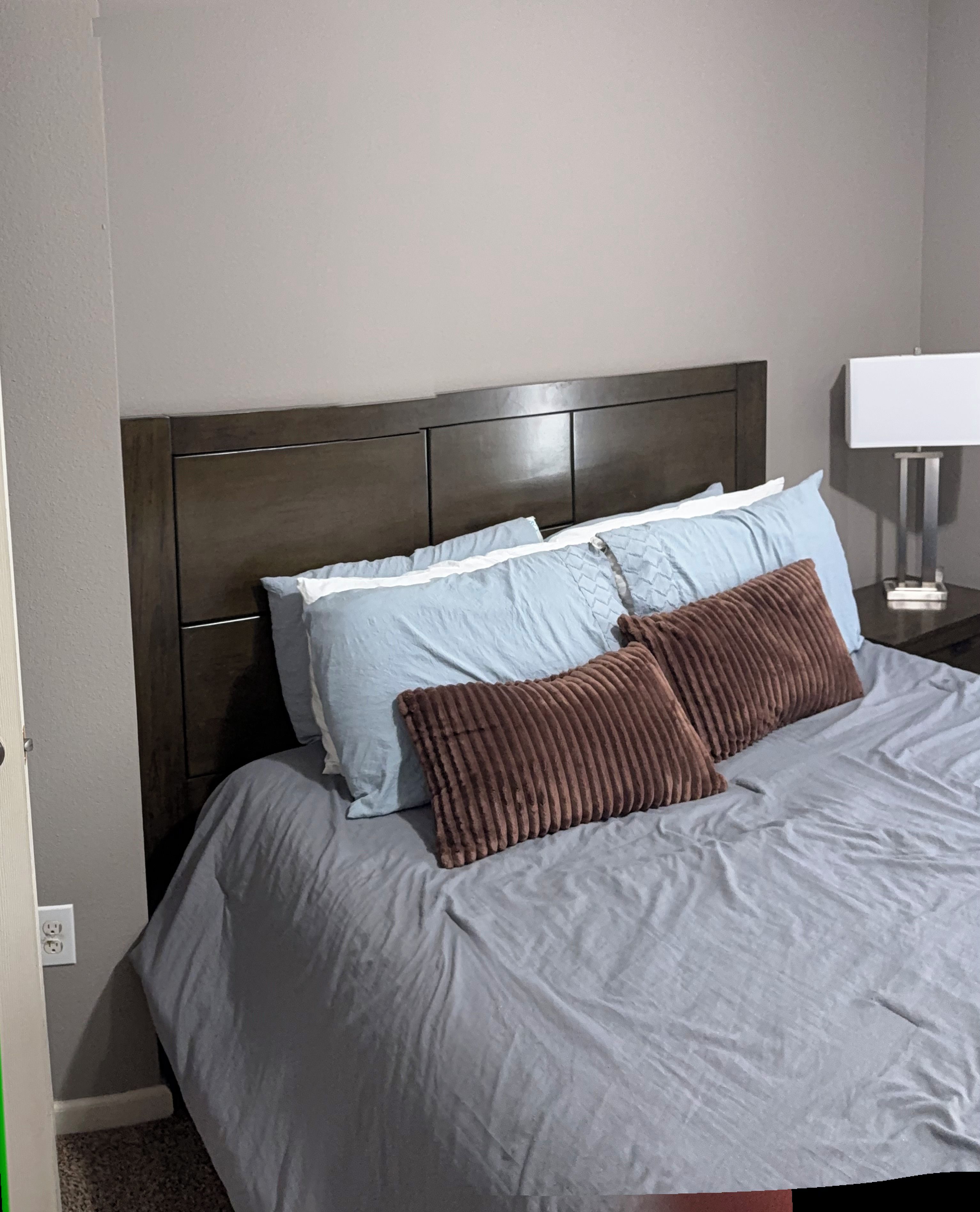 A bed with a headboard, pillows, and a bedside table with a lamp.