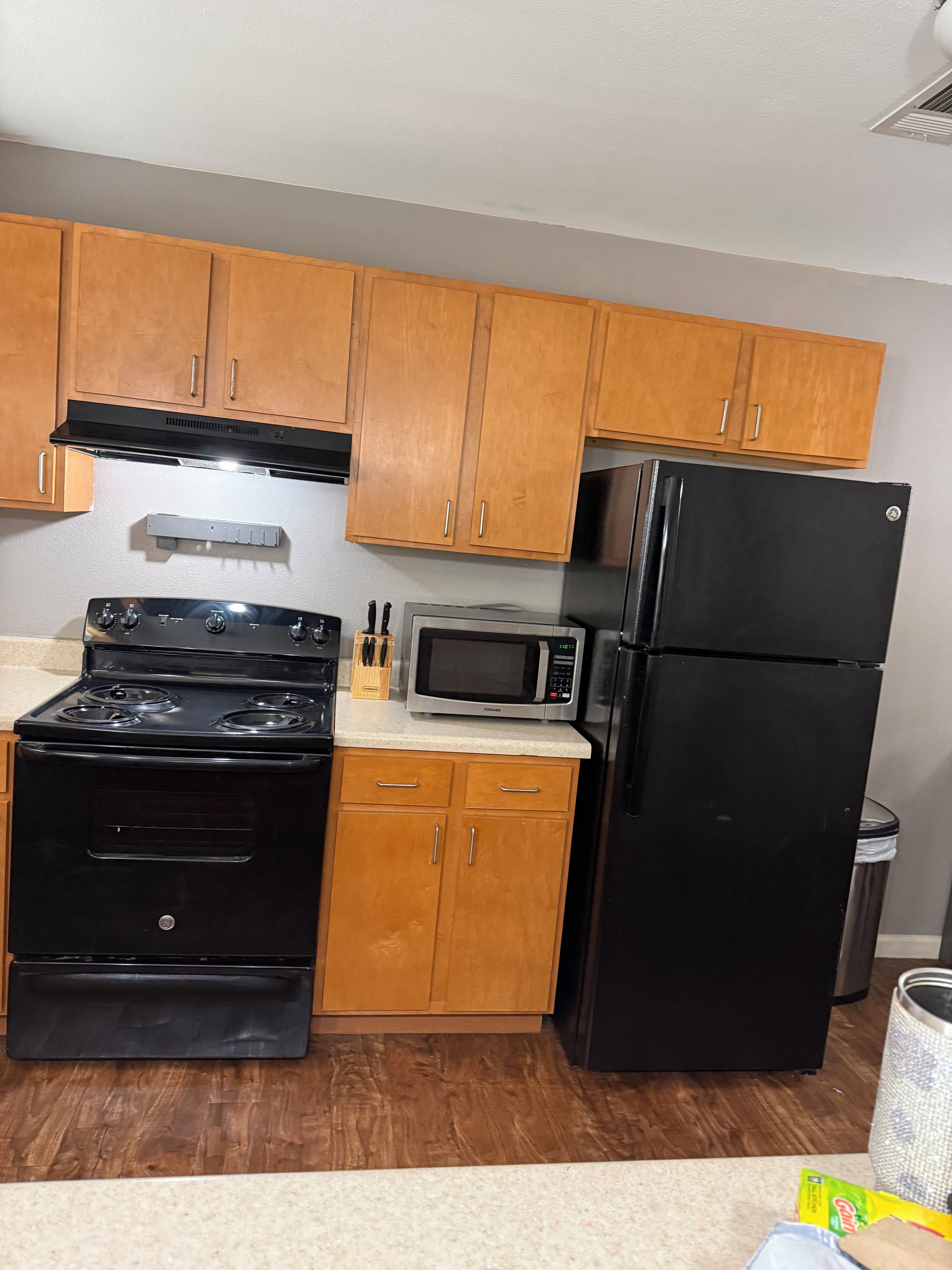 A kitchen with wooden cabinets, a black stove, a microwave, and a refrigerator.